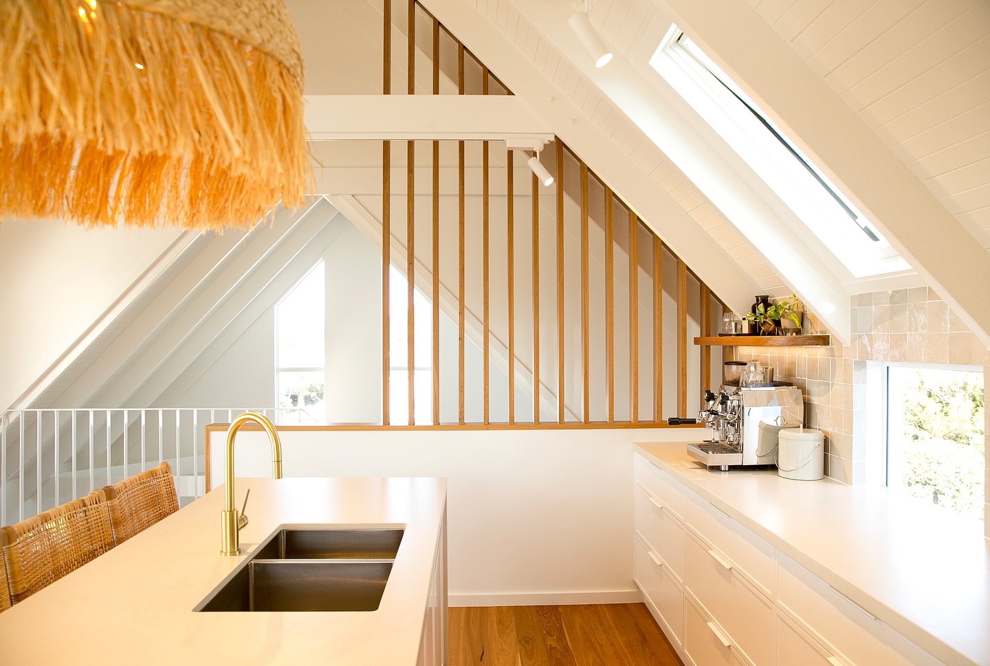 Kitchen island with brass tapware beneath a timber batten screen and skylight