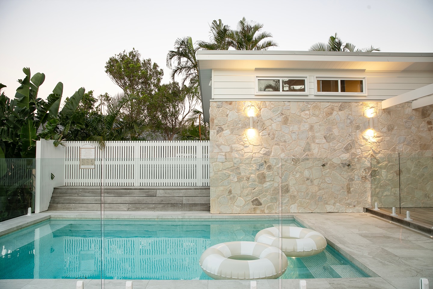 Pool terrace with a stacked stone wall, white battened screen and wall lights
