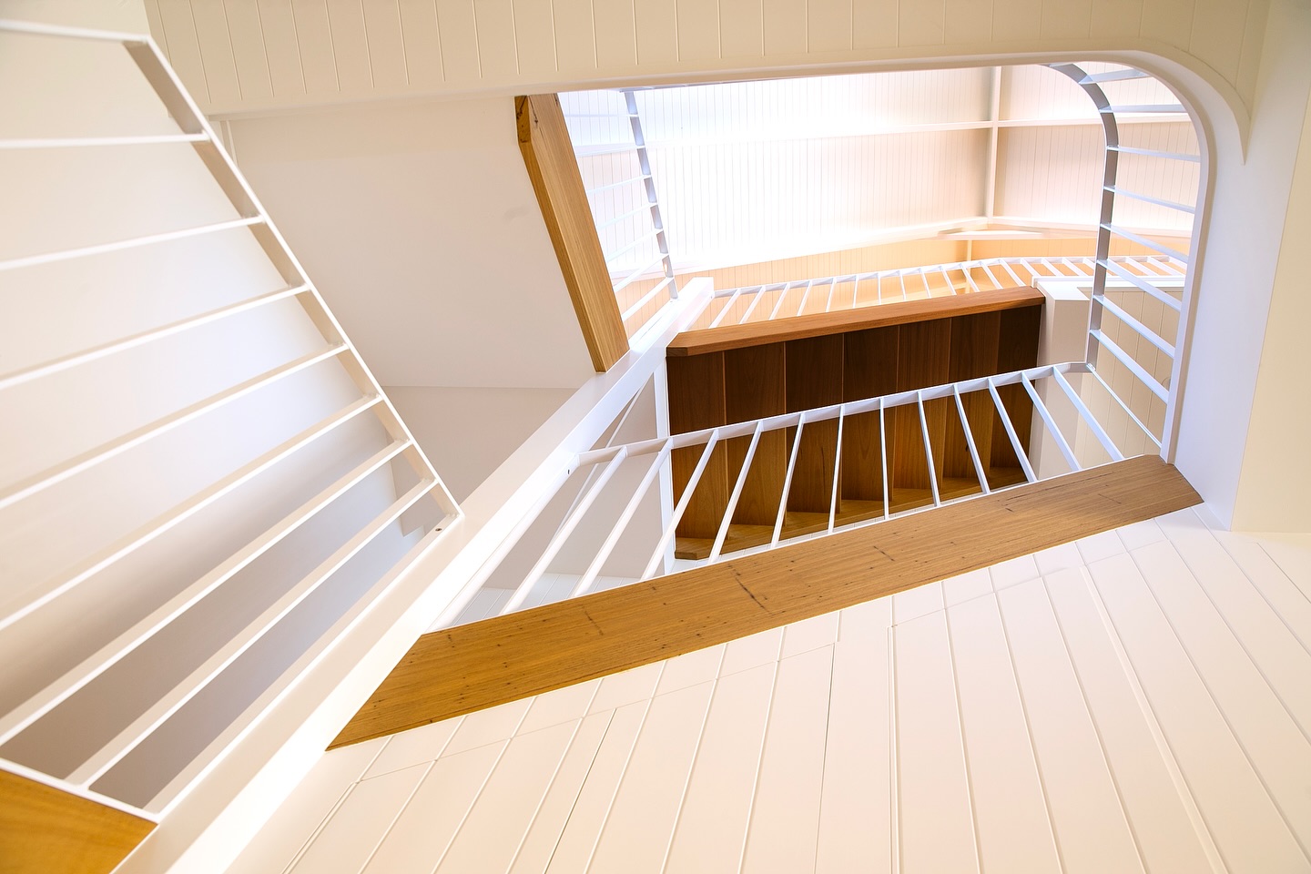 Looking down into a stair void with white balustrades and timber treads