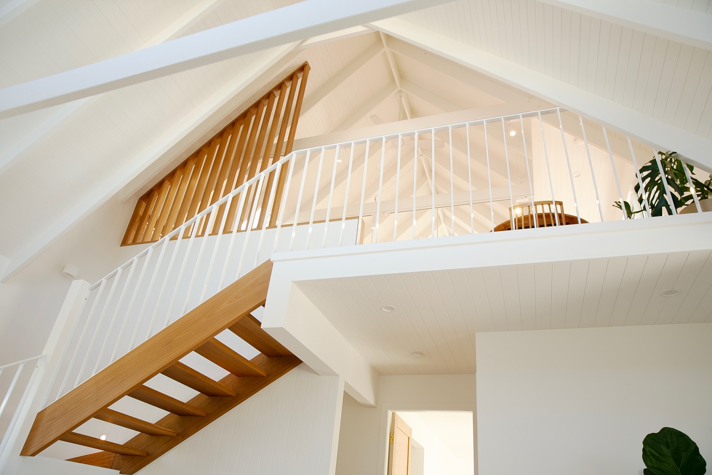 White vaulted ceiling with exposed beams and a timber-lined mezzanine balustrade